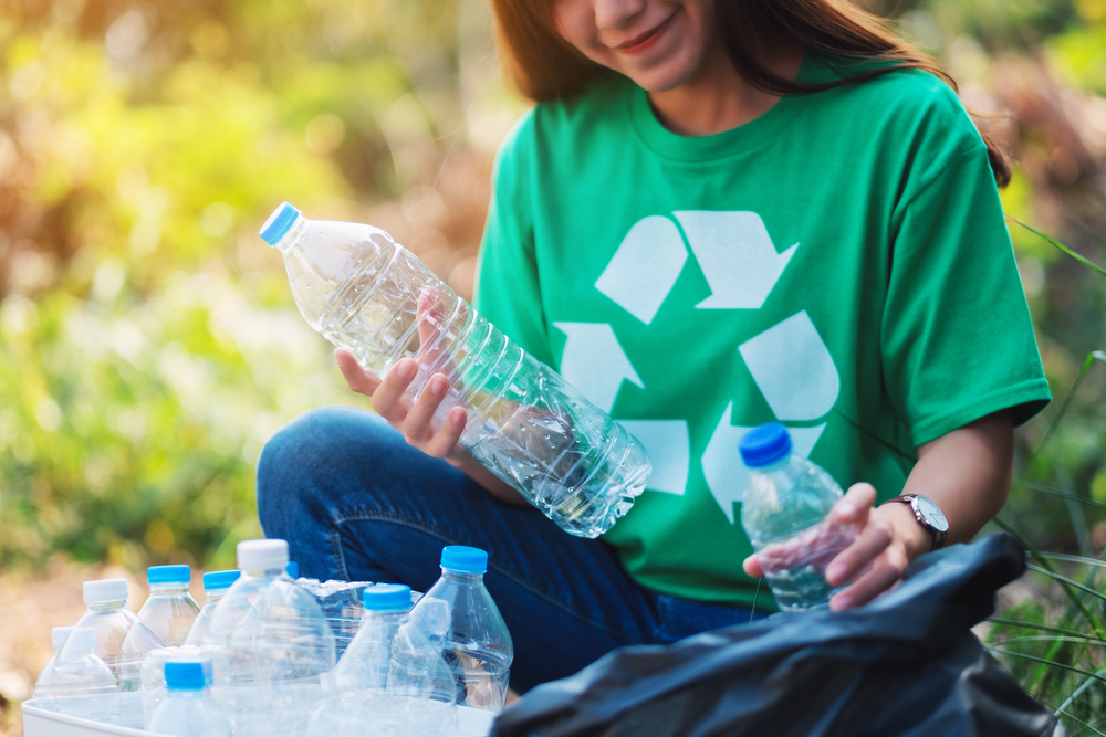 Young woman placing plastic bottles into a box for recycling